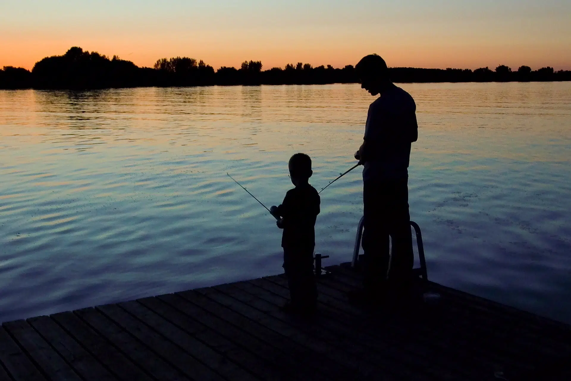 Père et son enfant pêchant sur un quai au coucher du soleil
