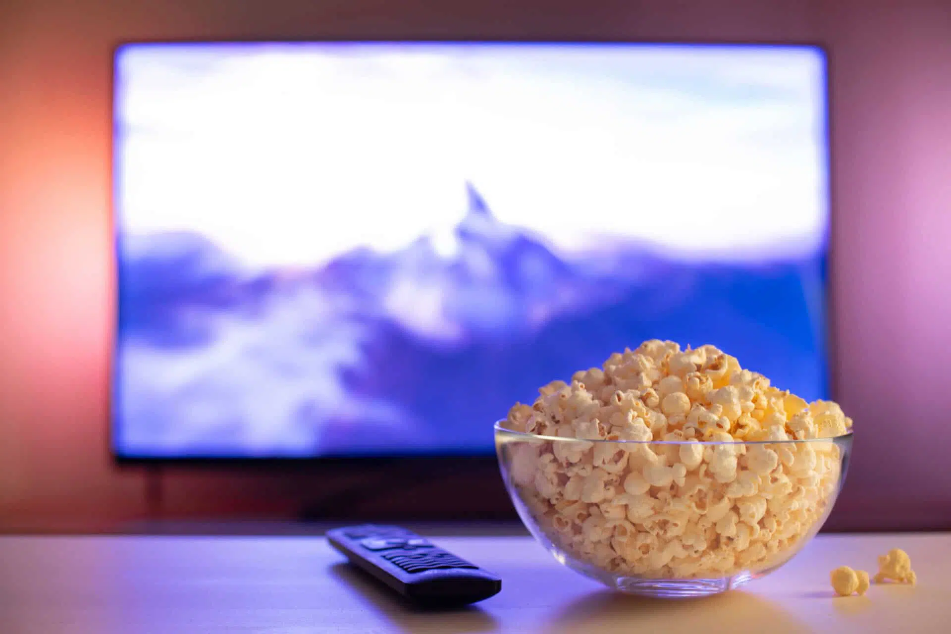 Bol de pop-corn disposé sur une table à côté d'une manette de télévision. En arrière-plan, on voit un écran de télévision qui diffuse un film.
