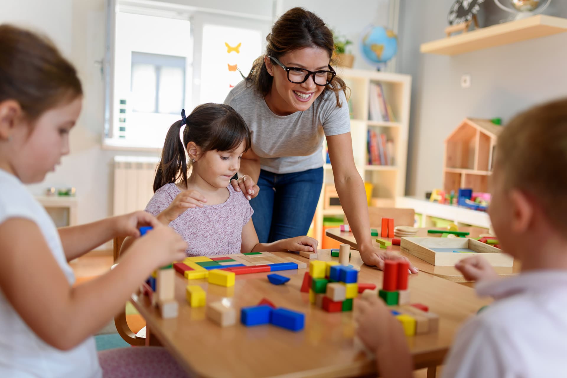 Trois enfants et leur éducatrice s'amusent avec des blocs autour d'une table.
