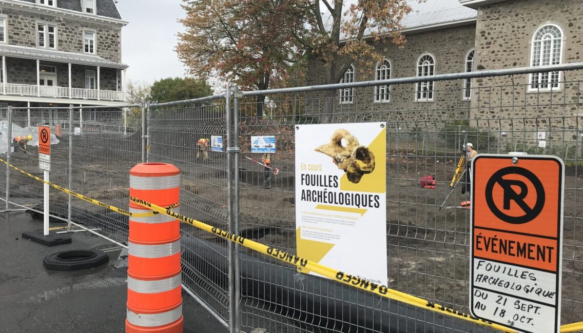 Personnes qui procèdent à des fouilles archéologiques dans le Vieux-Boucherville. On y voit aussi des grilles avec une pancarte sur laquelle il est inscrite : Fouilles archéologiques en cours.