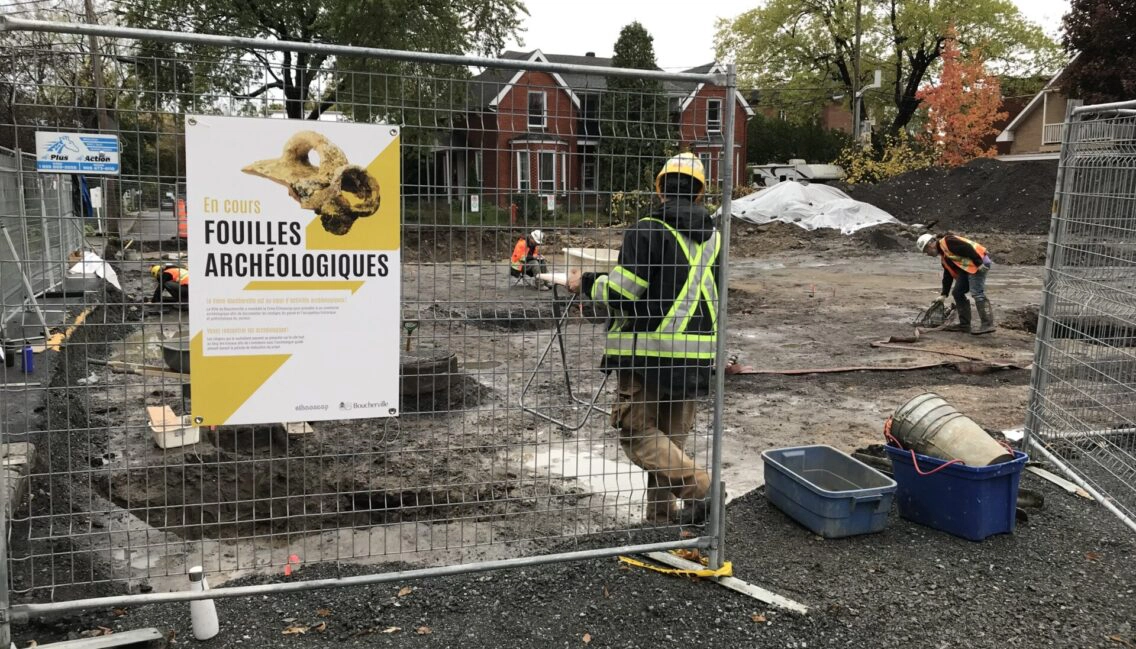 Personnes qui procèdent à des fouilles archéologiques dans le Vieux-Boucherville. On y voit aussi des grilles avec une pancarte sur laquelle il est inscrite : Fouilles archéologiques en cours.