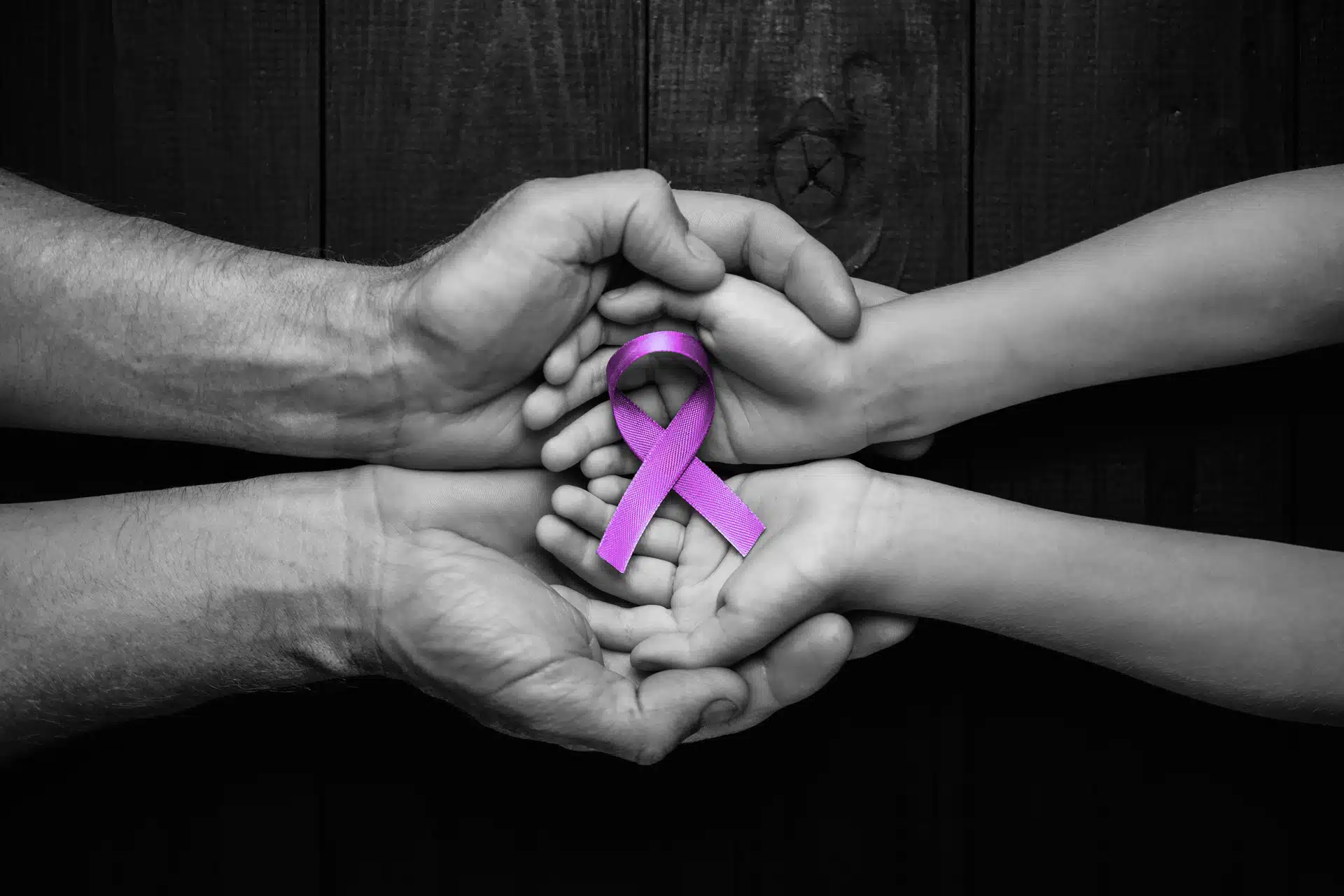 Mains d'homme et mains d'enfant qui s'unissent pour soutenir un ruban mauve