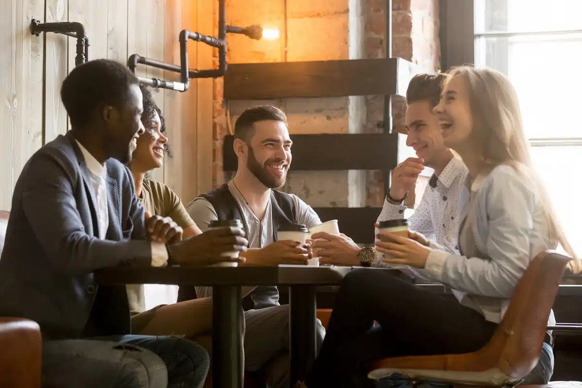 Cinq personnes de différentes nationalités discutent en prenant un café autour d'une table.