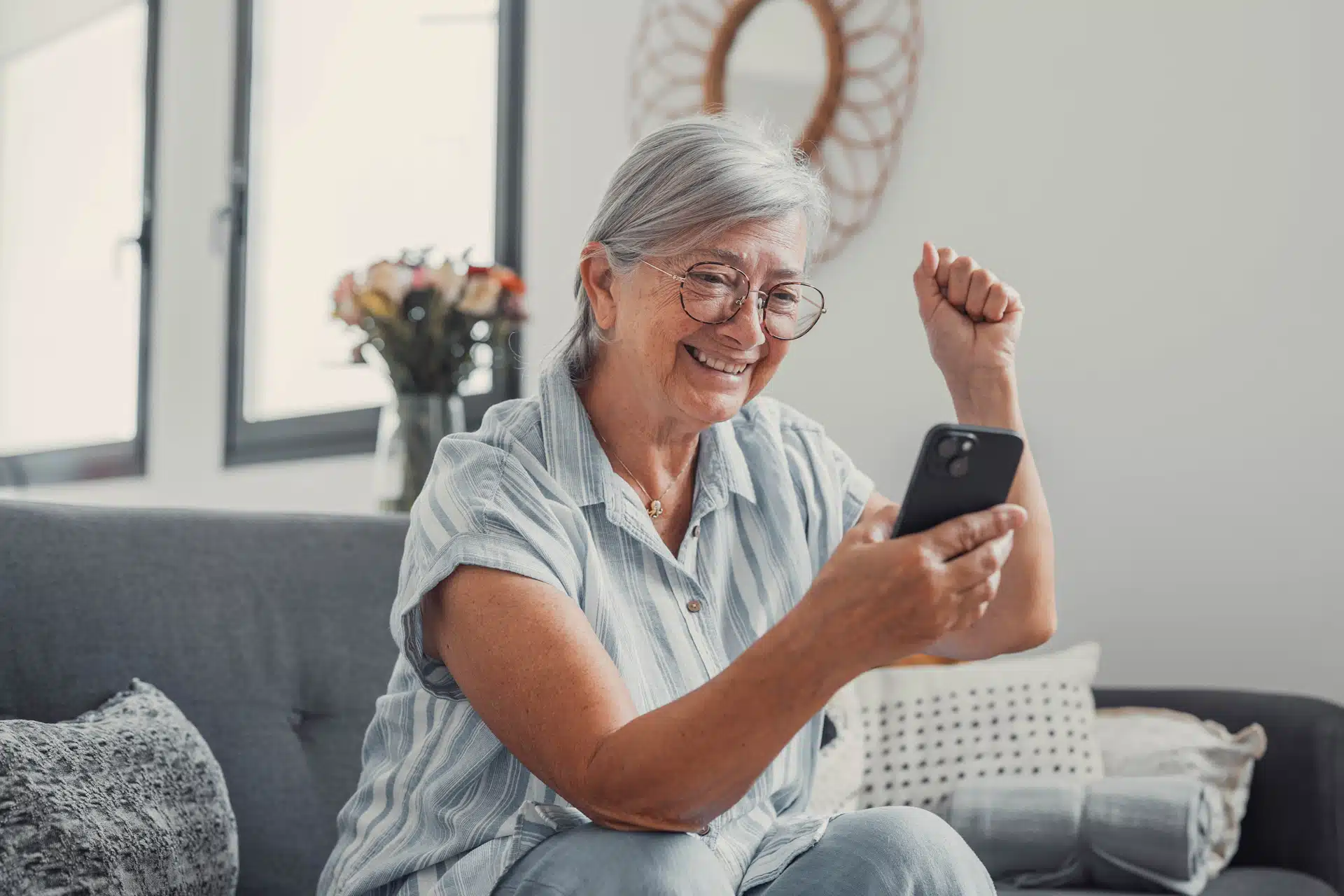 Femme aînée qui regarde son cellulaire, assise sur son divan.
